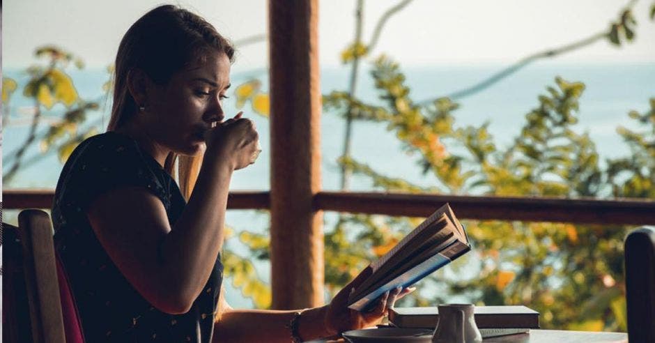 Una mujer joven toma café mientras lee un libro