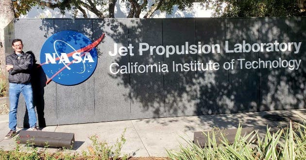 Un hombre adulto posa junto a un letrero que dice NASA