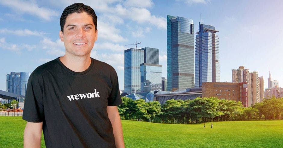 Un hombre con camiseta negra posa junto a la silueta de varios edificios