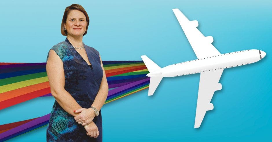 Una mujer con vestido azul posa frente a un avión blanco decorado con la bandera LGBT