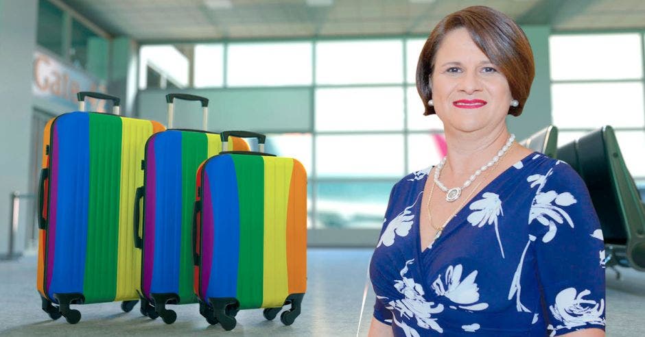 Una mujer de vestido azul posa junto a unas valijas de colores