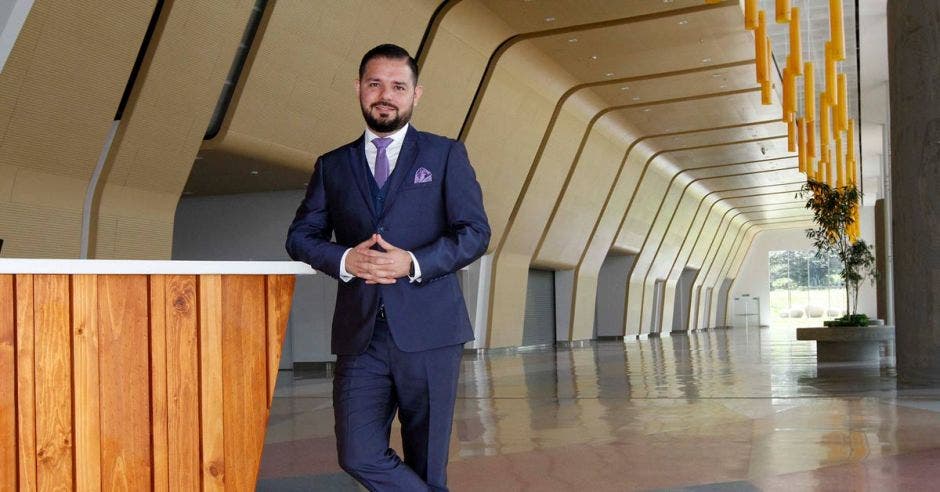 Un hombre con saco y corbata se apoya sobre un mostrador en el lobby de un centro de convenciones