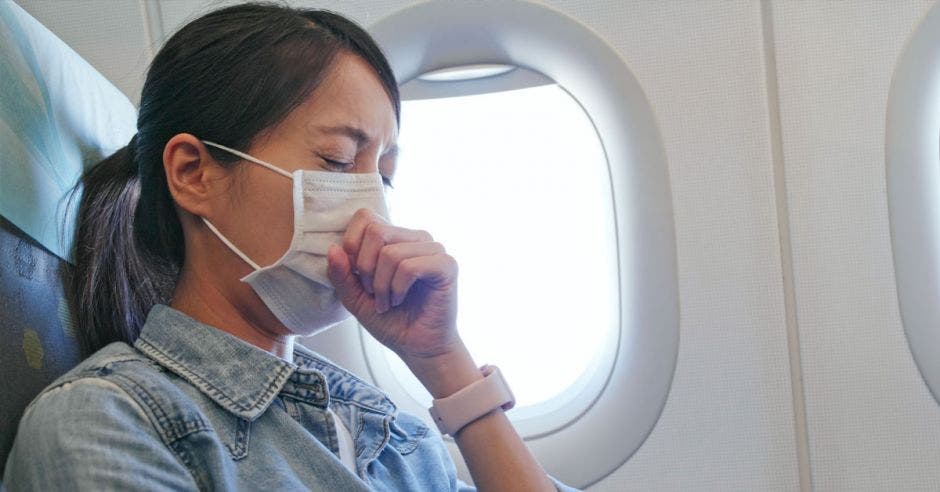 Mujer que se siente mal y que lleva mascarilla en el avión