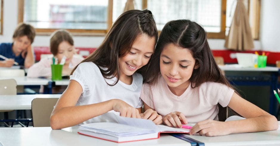 Dos niñas estudian con un cuaderno dentro de un salón de clases