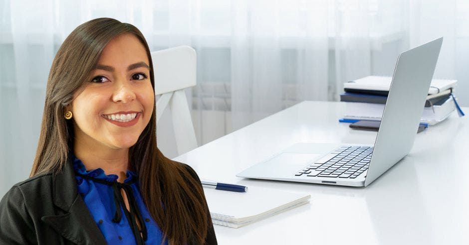 Un mujer posa junto a un escritorio y una computadora