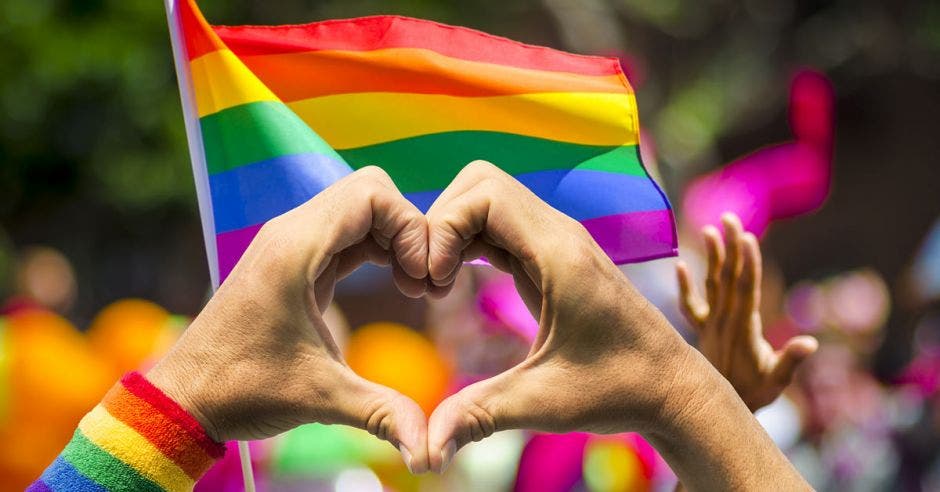 Bandera de la diversidad y persona haciendo símbolo de corazón