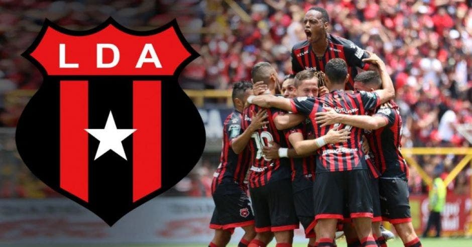 Jugadores de fútbol celebrando un gol con el escudo de Alajuelense de fondo