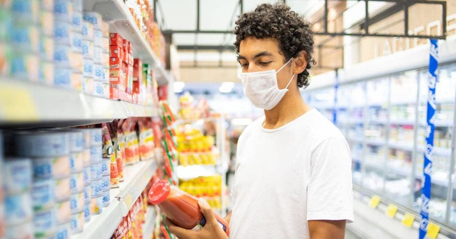 Un hombre con mascarilla compra salsa de tomate en el supermercado