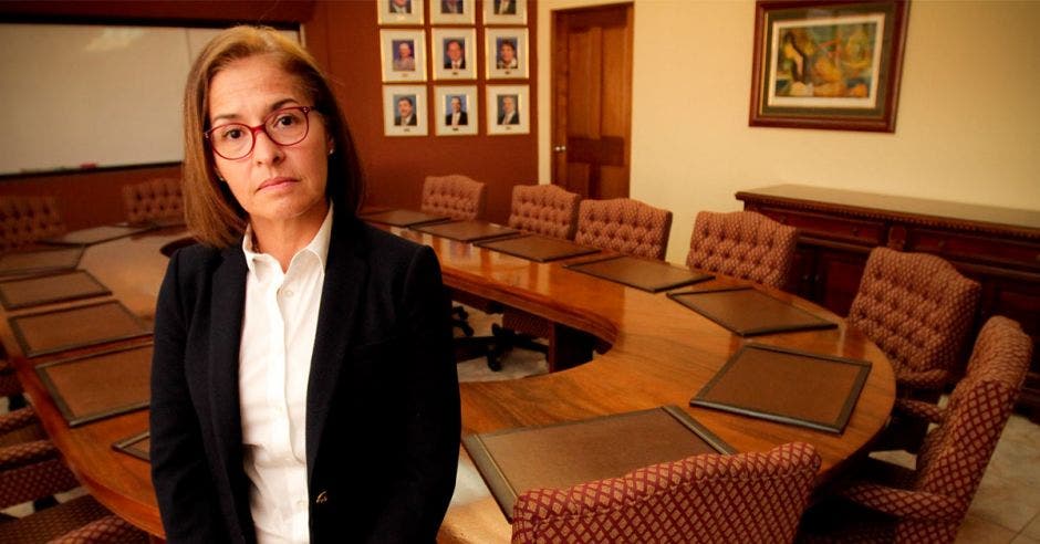 Mujer de lentes posa en una sala de reuniones con la mesa de fondo