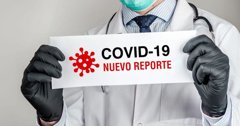 Hombre con bata y guantes sostiene papel con casos de Covid-19