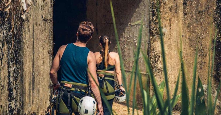 Una pareja heterosexual con ropa deportiva y cascos se adentran en una cueva de piedra