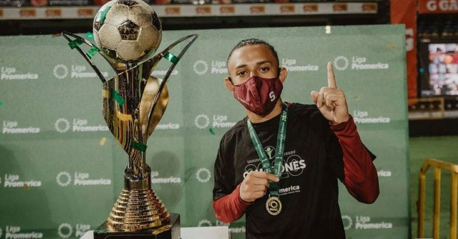 Jugador portando medalla posa junto a un trofeo