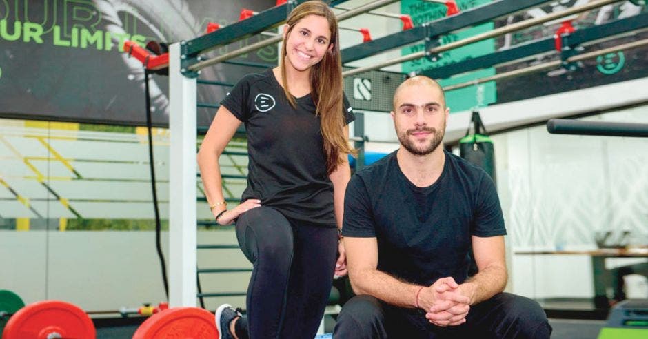 Dos personas, una de pie y otra sentada en gimnasio