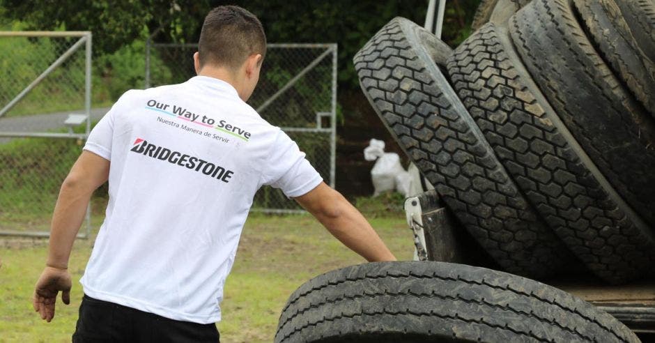 Vemos a una persona de espaldas con una camisa blanca que dice "Bridgestone" a la par de un montón de llantas.