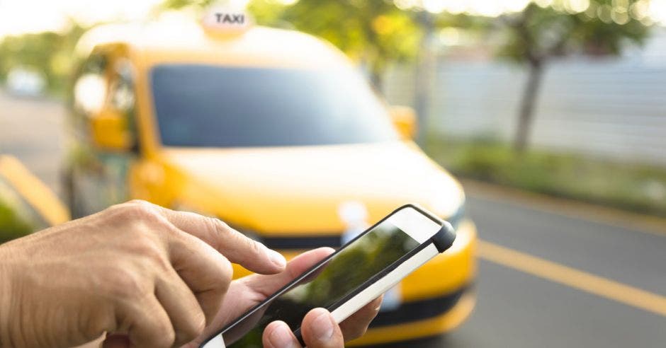 Vemos a alguien con un celular y detrás un taxi