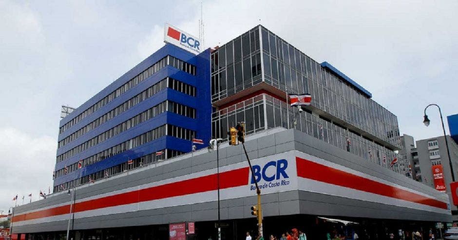 Fachada de un amplio edificio gris con detalles en banco, azul y rojo