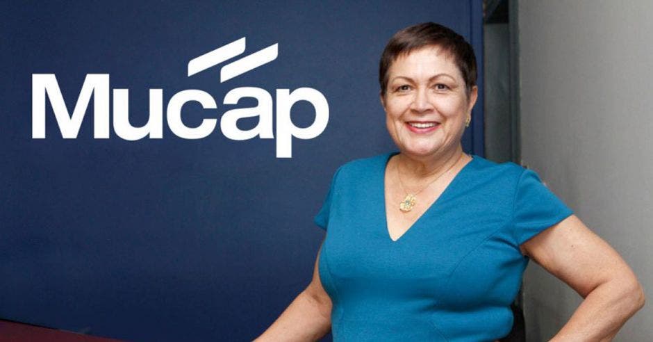 Vemos a una señora en un vestido azul enfrente del logo de Mucap