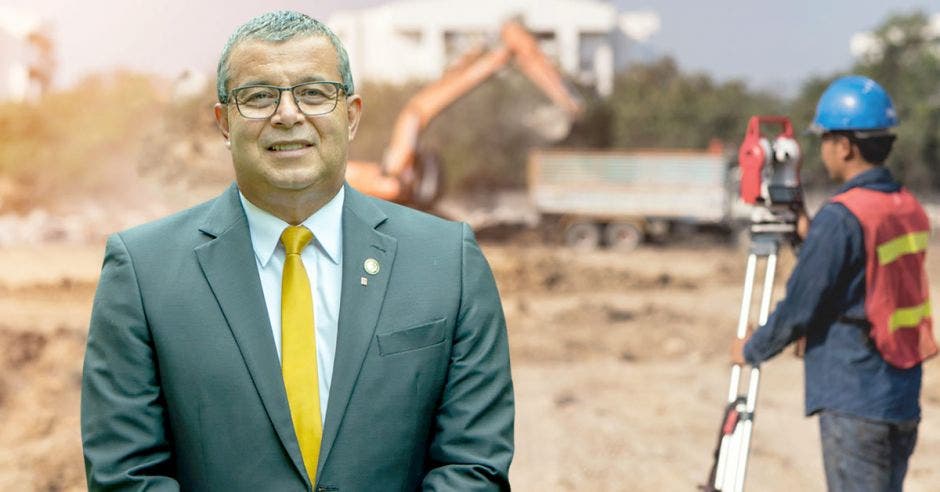 Un hombre de saco gris y corbata amarilla posa sobre un fondo de construcción