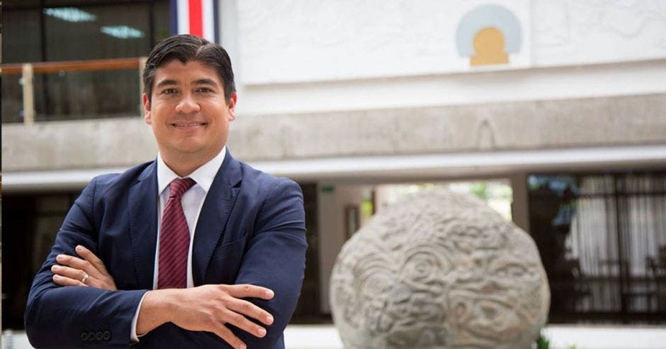 Hombre de traje y brazos cruzados frente a piedra.