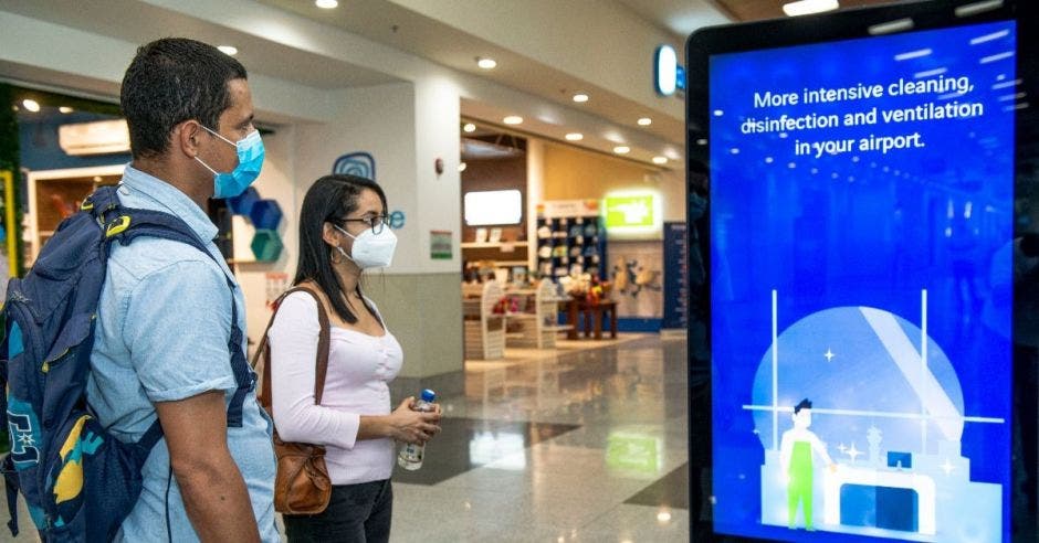 Un hombre y una mujer observan un mupi con instrucciones para el dsitanciamiento físico