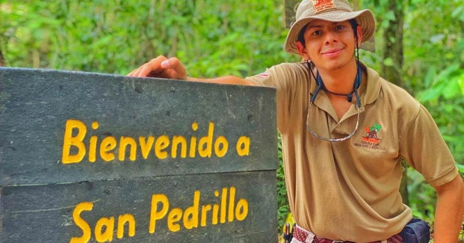 Un joven se apoya sobre un letrero que dice Bienvenido a San Pedrillo