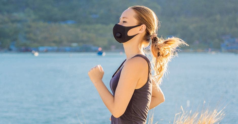 Una mujer con una mascarilla negra corre junto a un lago