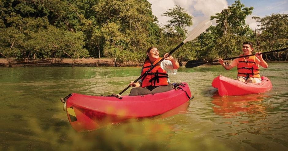 dos jóvenes cruzan un río a bordo de un kayak rojo