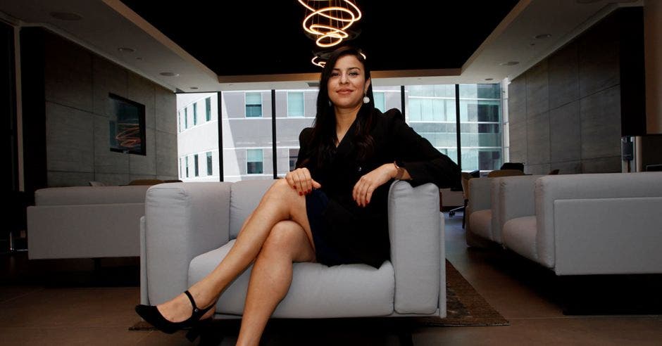 una mujer con vestido ejecutivo negro se sienta sobre un sillón gris
