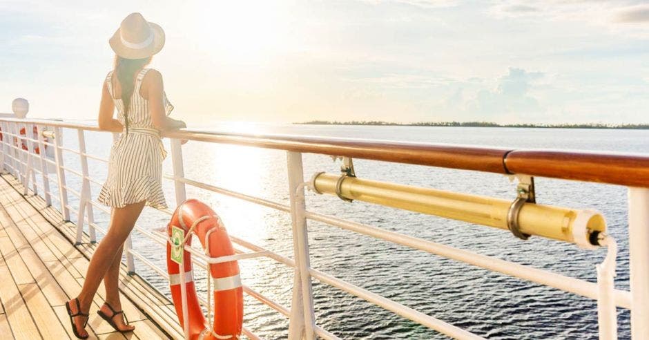 Una turista se apoya sobre la baranda de un crucero, mirando un atardecer