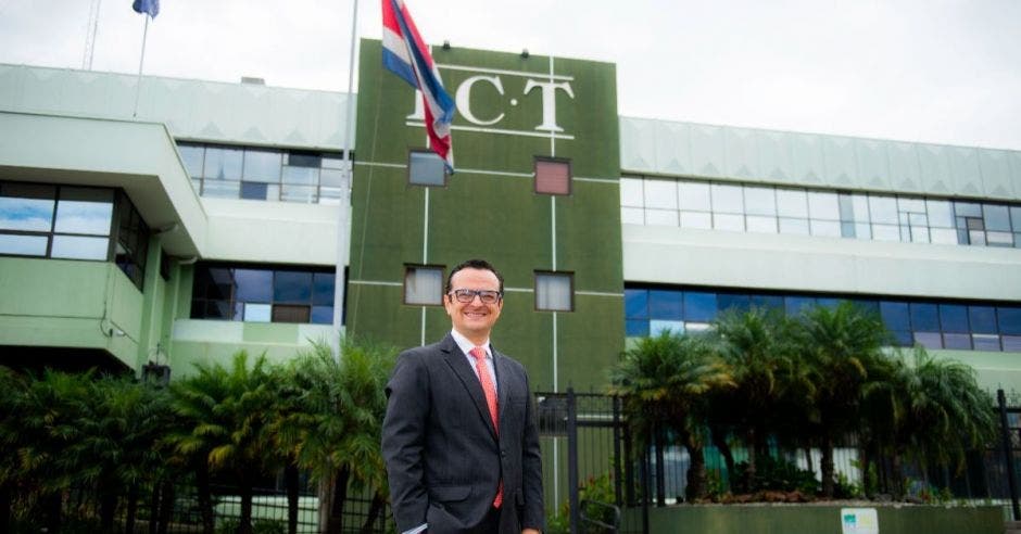 Un hombre de saco y corbata posa junto a un edificio de color verde