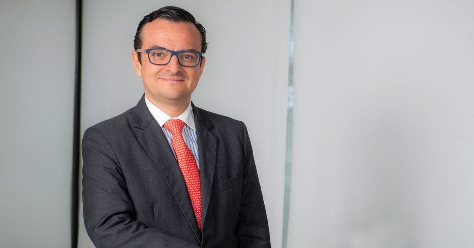 Un hombre con anteojos, vestido de traje oscuro y corbata roja