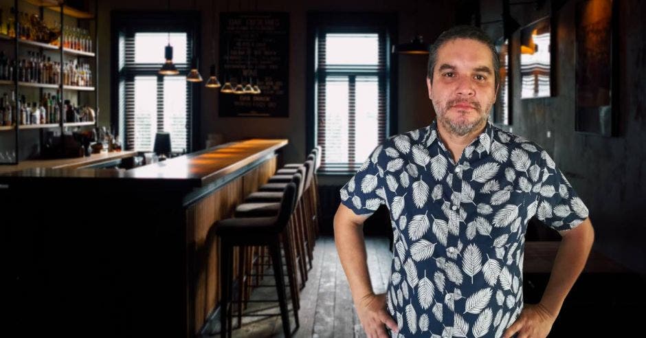 un hombre con camisa floreada parado junto a la barra de un bar