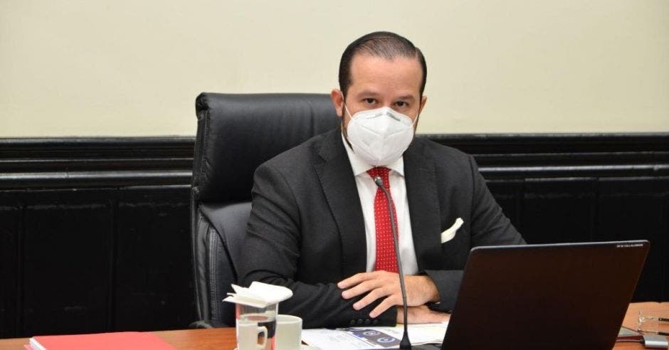 Un hombre con pelo corto, corbata roja, traje y mascarilla