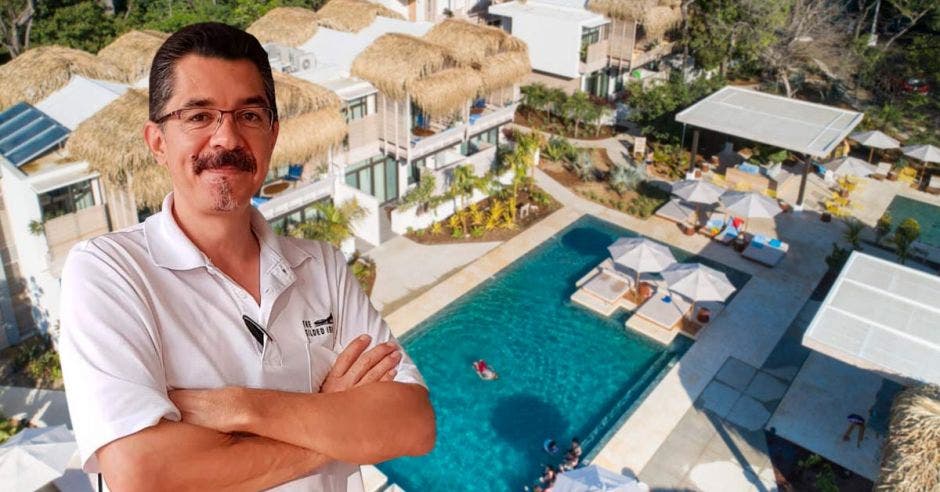 Un hombre de bigote y camisa blanca posa sobre la imagen de un hotel