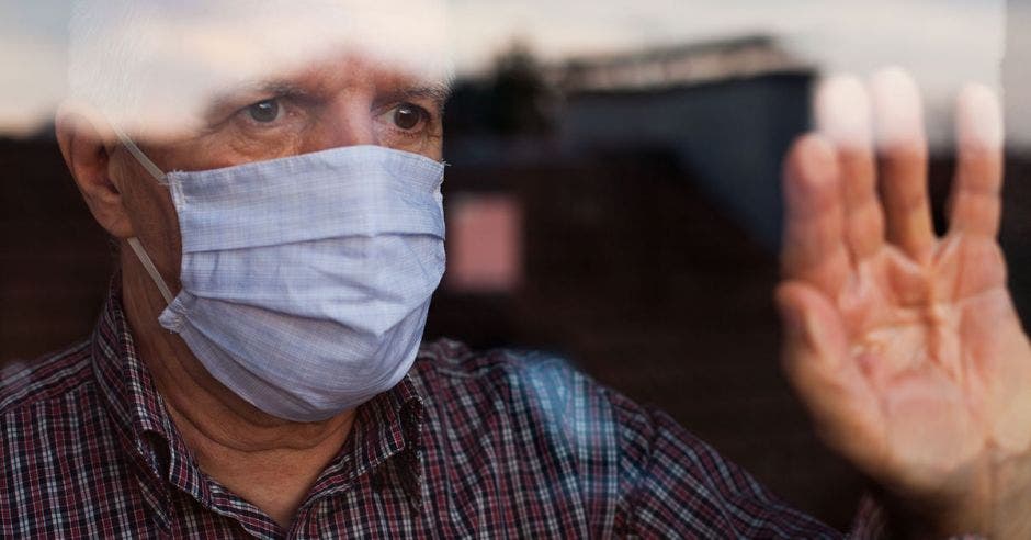 señor de la tercera edad vusando mascarilla viendo a través de la ventana