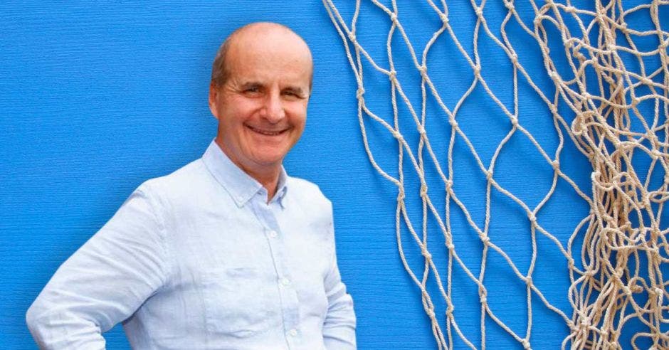 un hombre calvo sonriendo sobre un fondo azul y una red de arrastre