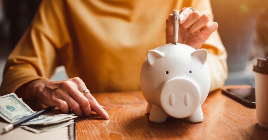 mujer depositando un billete a alcancía de cerdito