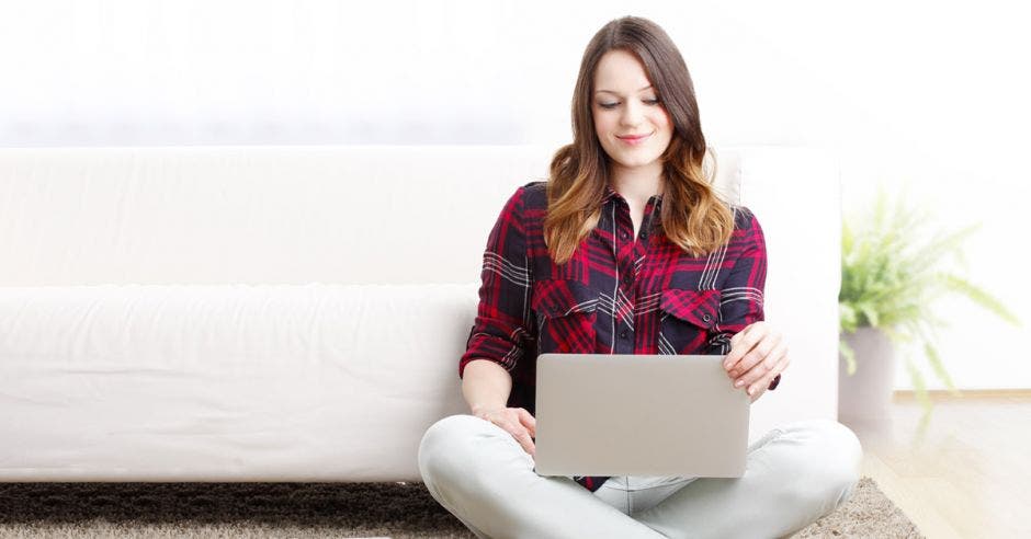 muchacha sentada en un sollón viendo su laptop
