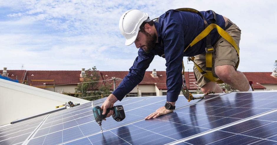 un hombre instala un panel solar en el techo de una casa