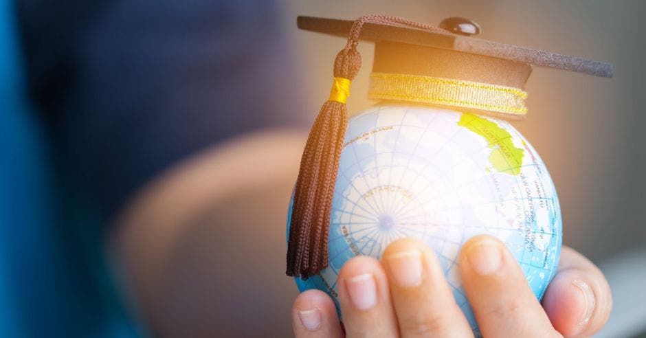 Un globo terráqueo con un birrete de graduación encima, sobre una mano