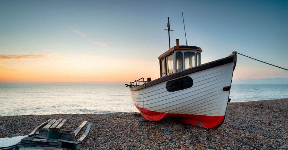 un barco pesquero color blanco con rojo, encallado en una playa