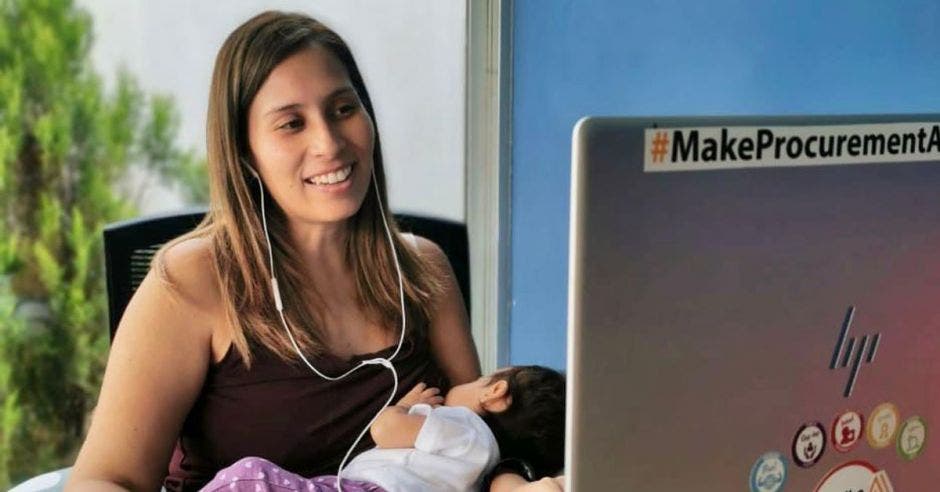 una mujer chinea a su bebe mientras realiza tareas frente a una computadora