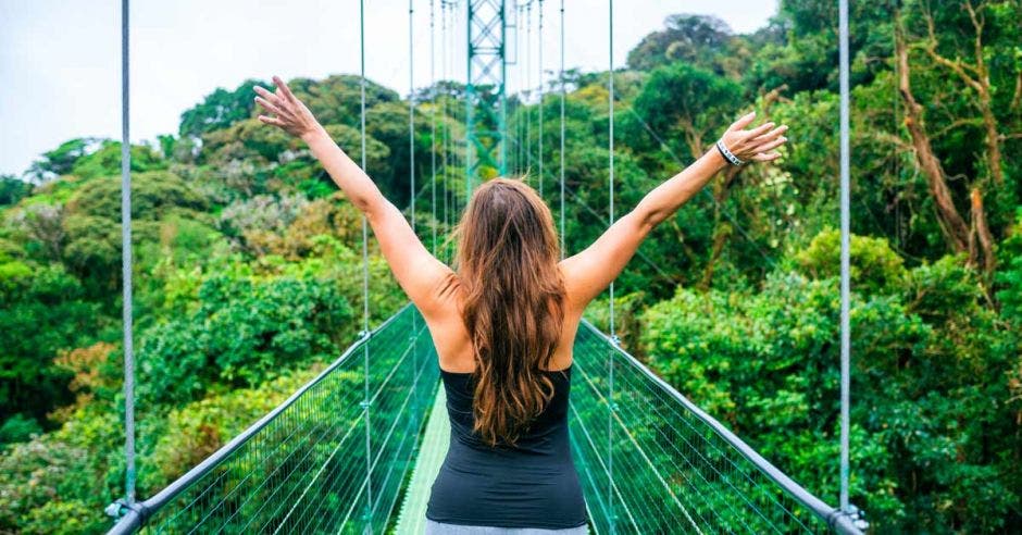 Una mujer con los brazos abiertos al cielo sobre un puente verde