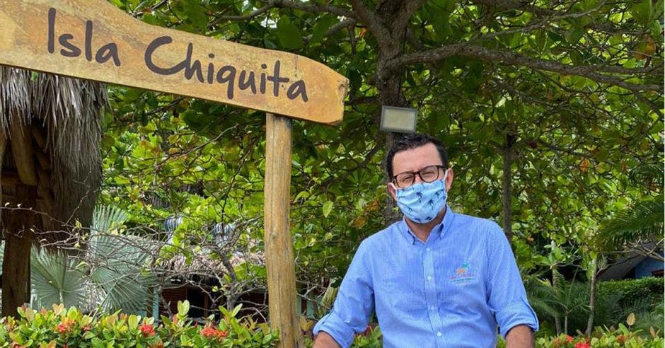 un hombre de camisa celeste y mascarilla posa junto a un letrero que dice Isla Chiquita