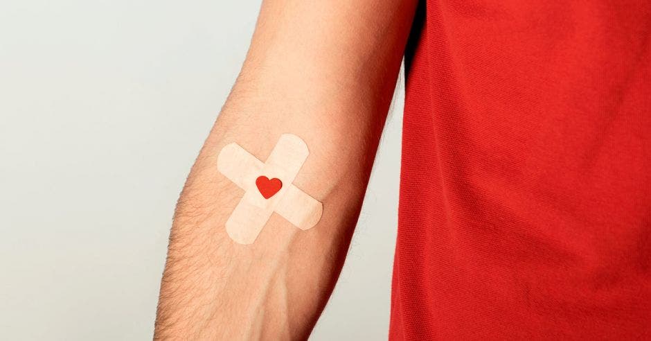 un joven de camisa roja con una marca del pinchazo de una inyección