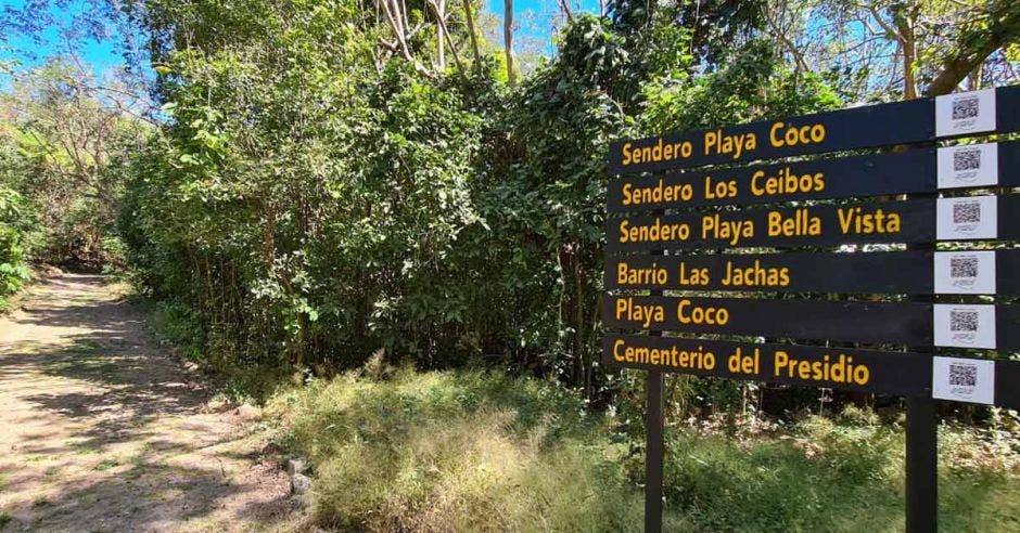 un letrero negro con letras amarillas a la orilla de un sendero