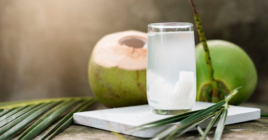 vaso con agua de coco y trozos de coco sobre una mesa blanca