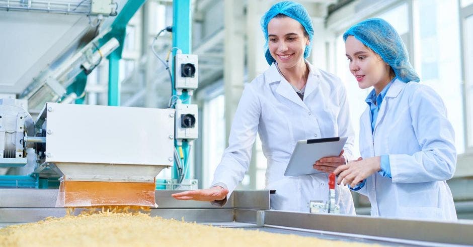 dos mujeres con bata y gorra trabajando en una fábrica de alimentos