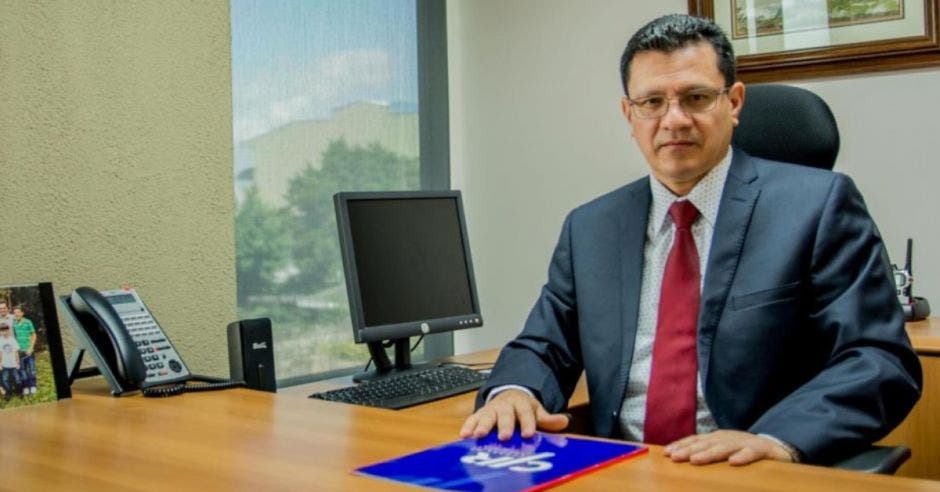 un hombre con saco oscuro y corbata roja sentado sobre un escritorio