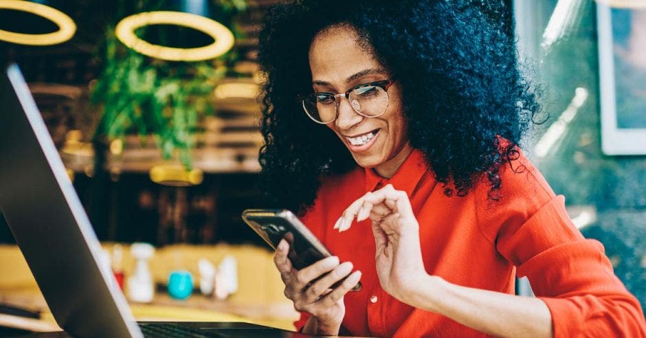 mujer de cabello negro con lentes  blusa naranja usando su celular